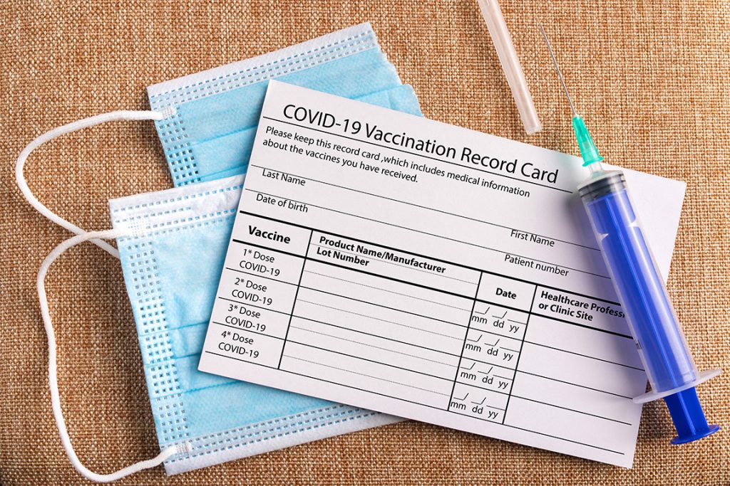 Coronavirus vaccination record card. Surgical mask divided into two parts and syringe. Concept of defeating Covid-19